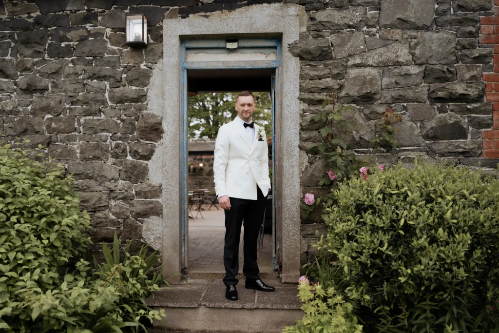The groom David standing in the stone doorway of the Coach House at Hillmount House wedding venue Northern Ireland.